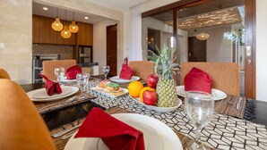 A dining table set with plates, glasses, and a fruit bowl containing apples, oranges, and a pineapple. - Villa Amerta by Taman Bali (Ungasan)
