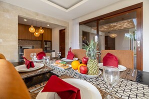 A dining table set with plates, glasses, and a fruit bowl containing apples and a pineapple. - Villa Amerta by Taman Bali (Ungasan)