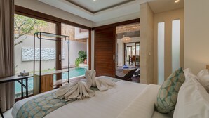 A hotel room with a large bed, a view of a swimming pool, and a balcony with a wooden railing. - Villa Amerta by Taman Bali (Ungasan)