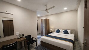 Una habitación de hotel con cama, escritorio, silla, armario y zona de ducha.