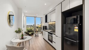 Eine moderne Küche mit einem schwarzen Kühlschrank, ein Essbereich mit Tisch und Stühlen und ein großes Fenster mit Blick auf die Stadt.