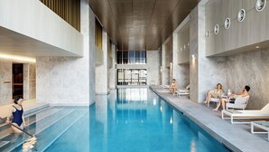 Ein moderner, überdachter Pool mit klarem, blauem Wasser, umgeben von Sitzbereichen und einer hohen Decke mit eingelassener Beleuchtung.