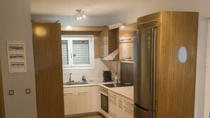 Una cocina moderna con armarios de madera, un refrigerador de acero inoxidable y un ventanal con persianas.
