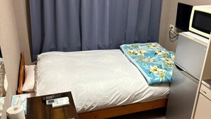 Quarto pequeno e bem organizado com cama, escrivaninha, geladeira e televisão.