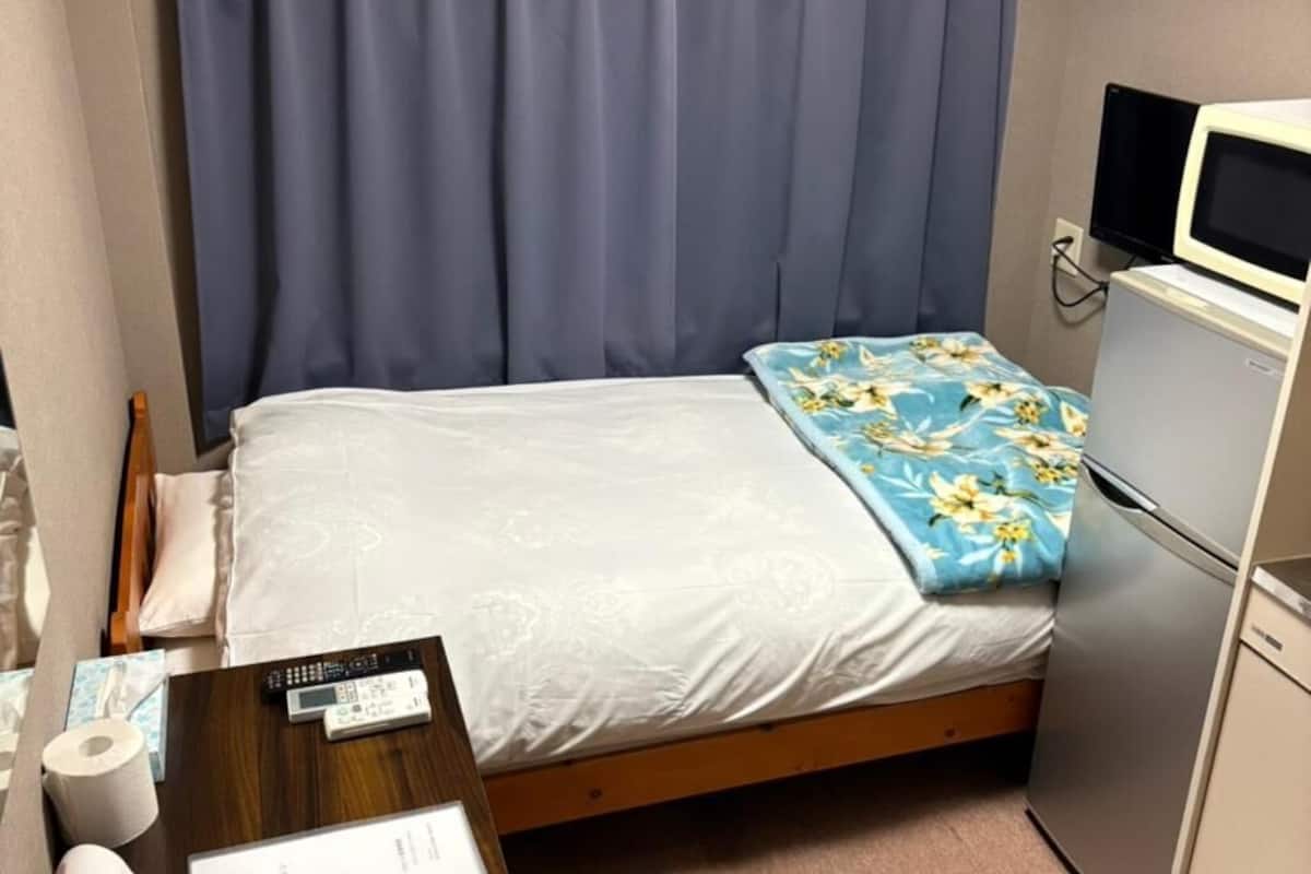 Une petite chambre à coucher, bien rangée, avec un lit, un bureau, un réfrigérateur et un téléviseur.