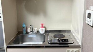 Uma cozinha compacta com uma pia de aço inoxidável, um fogão pequeno e uma prateleira sobre a pia com uma panela e um objeto decorativo.