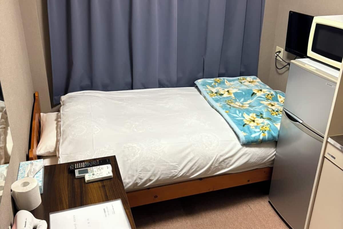 Une petite chambre d’hôtel comprenant un lit, un bureau avec un ordinateur, un four à micro-ondes et un réfrigérateur.