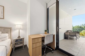 Ein Hotelzimmer mit Bett, Schreibtisch, Stuhl, Nachttisch, Lampe, einer kleinen Pflanze und einem Balkon mit Gartenmöbeln.