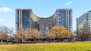 Een modern meerlaags gebouw met een gebogen gevel, omgeven door een grasrijk park met bomen en banken.
