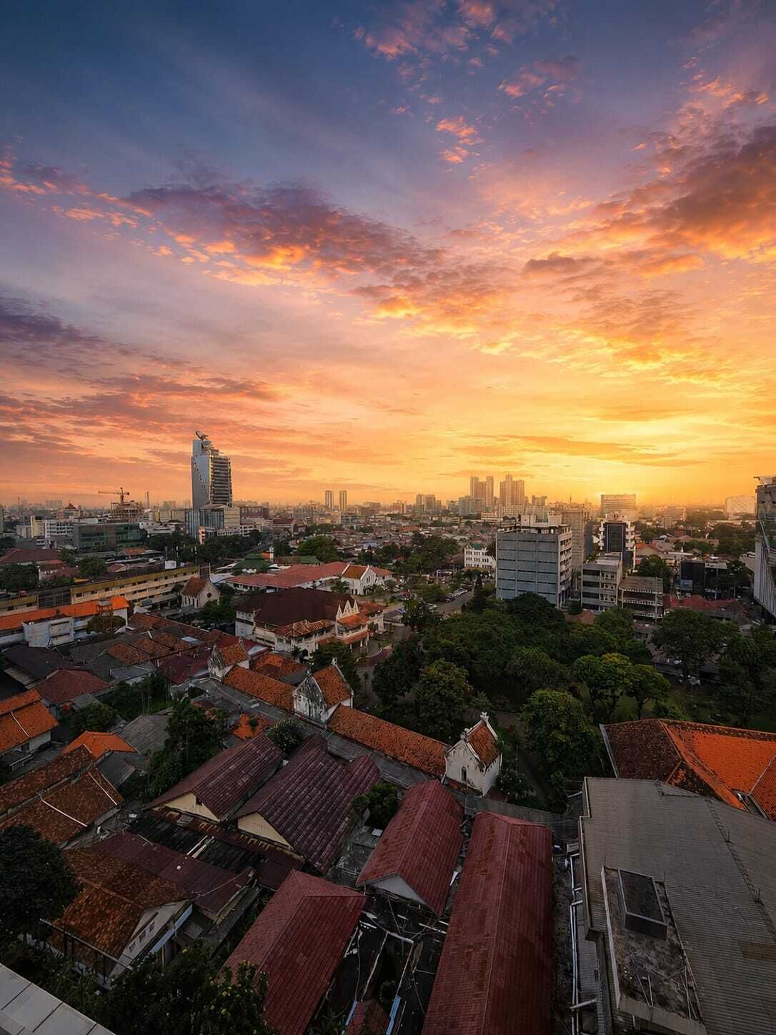 Paisagem urbana com mistura de edifícios modernos e tradicionais, um arranha-céu em destaque e um céu ao pôr do sol.