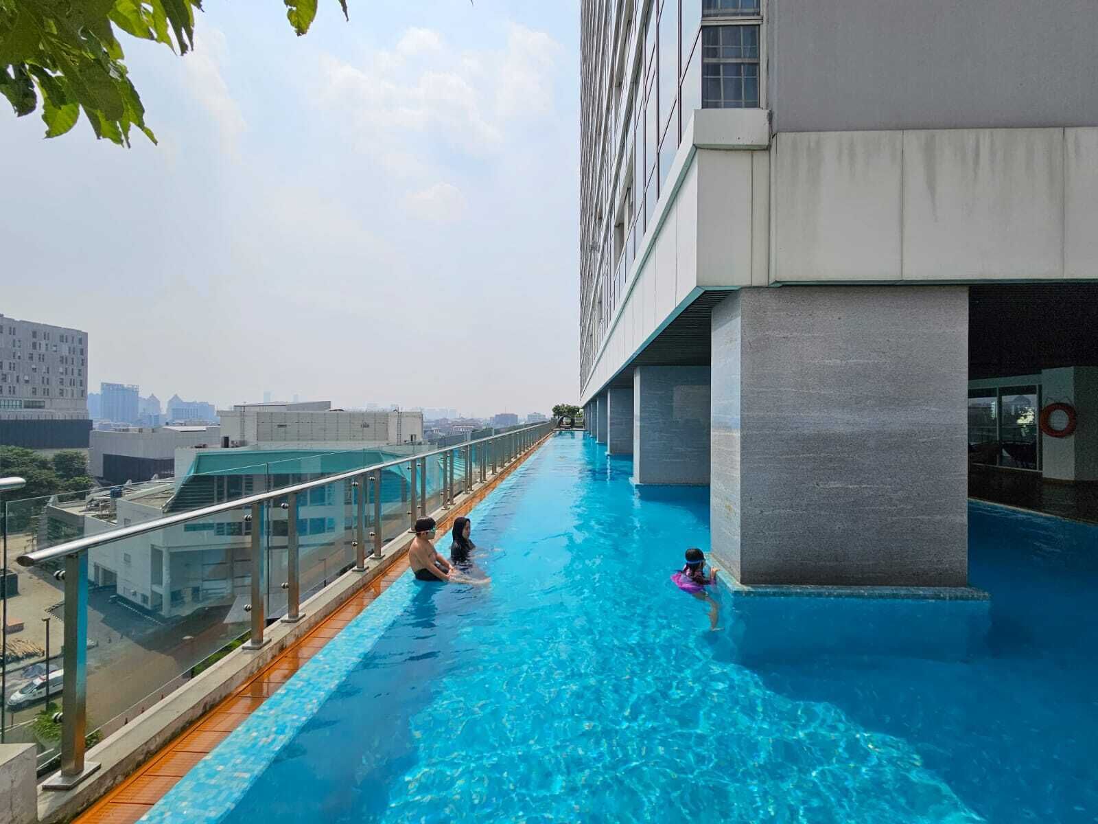 Ein Infinity-Pool auf dem Dach mit Glasgeländern, freier Blick auf die Stadtlandschaft und ein modernes Gebäude.