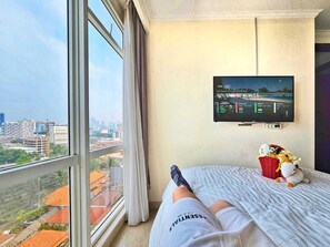 Une chambre d’hôtel avec une grande fenêtre, un lit, une télévision et une vue sur le paysage urbain.