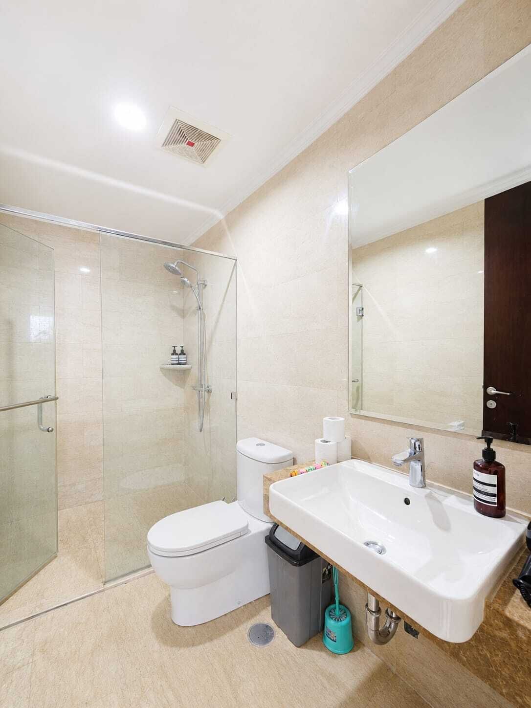 Un baño moderno con cabina de ducha de vidrio, inodoro blanco, lavamanos con espejo y un cubo de basura.