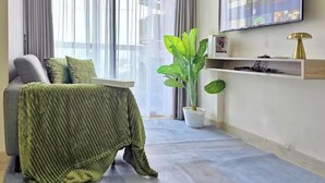 Uma sala de estar moderna com sofá, manta verde, planta em vaso e televisão na parede.