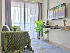 Una sala de estar moderna con un sofá, una manta verde, una planta en maceta y un televisor montado.