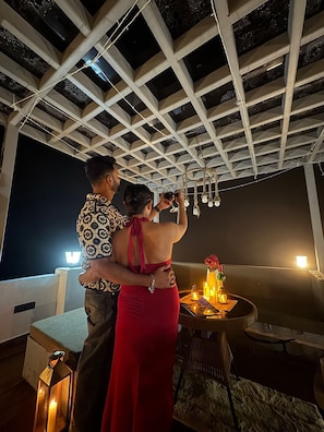 A couple embracing under a ceiling with a geometric pattern, a table with candles, and a bottle of liquor.