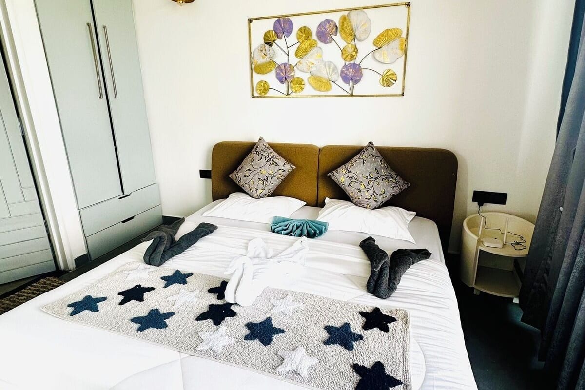 A neatly made bed with a star-patterned blanket, a wall-mounted floral artwork, and a bedside table with a lamp.