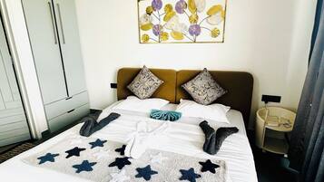 Una cama bien hecha con una manta estampada con motivos de estrellas, una obra de arte floral en la pared y una mesita de noche con una lámpara.