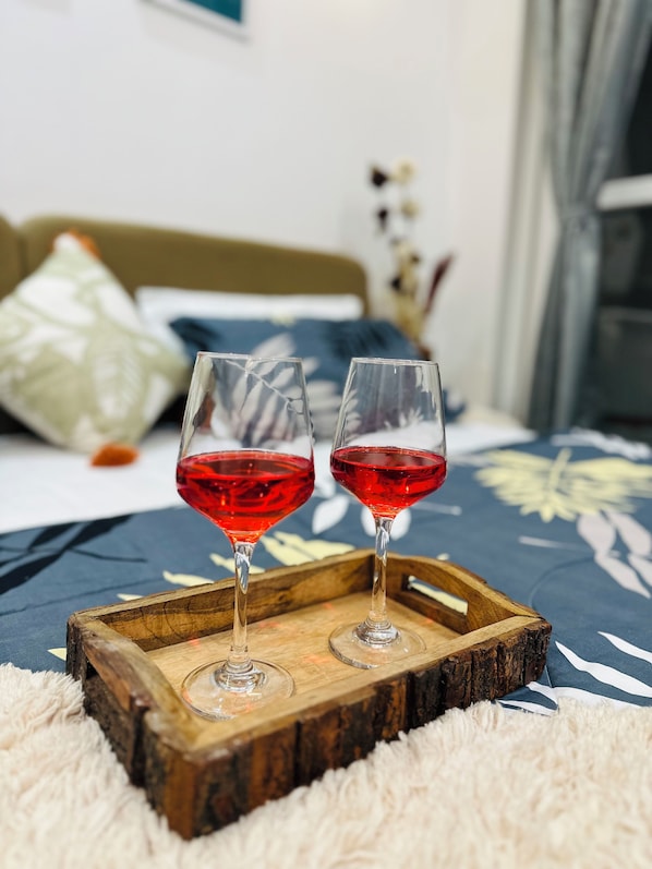 Two glasses of red wine on a wooden tray on a bed with a floral bedspread. - Advaya Stays - A Luxury Retreat (Dhari)