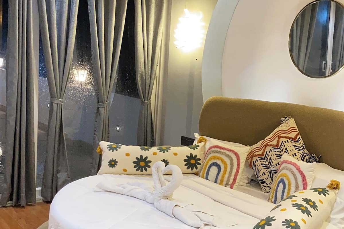 A circular bed with a round headboard, a round mirror, and multiple pillows with floral patterns.