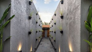 A corridor with a central pathway flanked by walls with potted plants and lights, leading to a building with a tiled roof. - The Clifton Villas Ubud (Ubud)