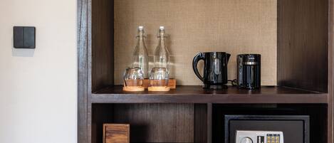 A wooden shelf with glass bottles, a black coffee maker, a safe, and two white cups.
