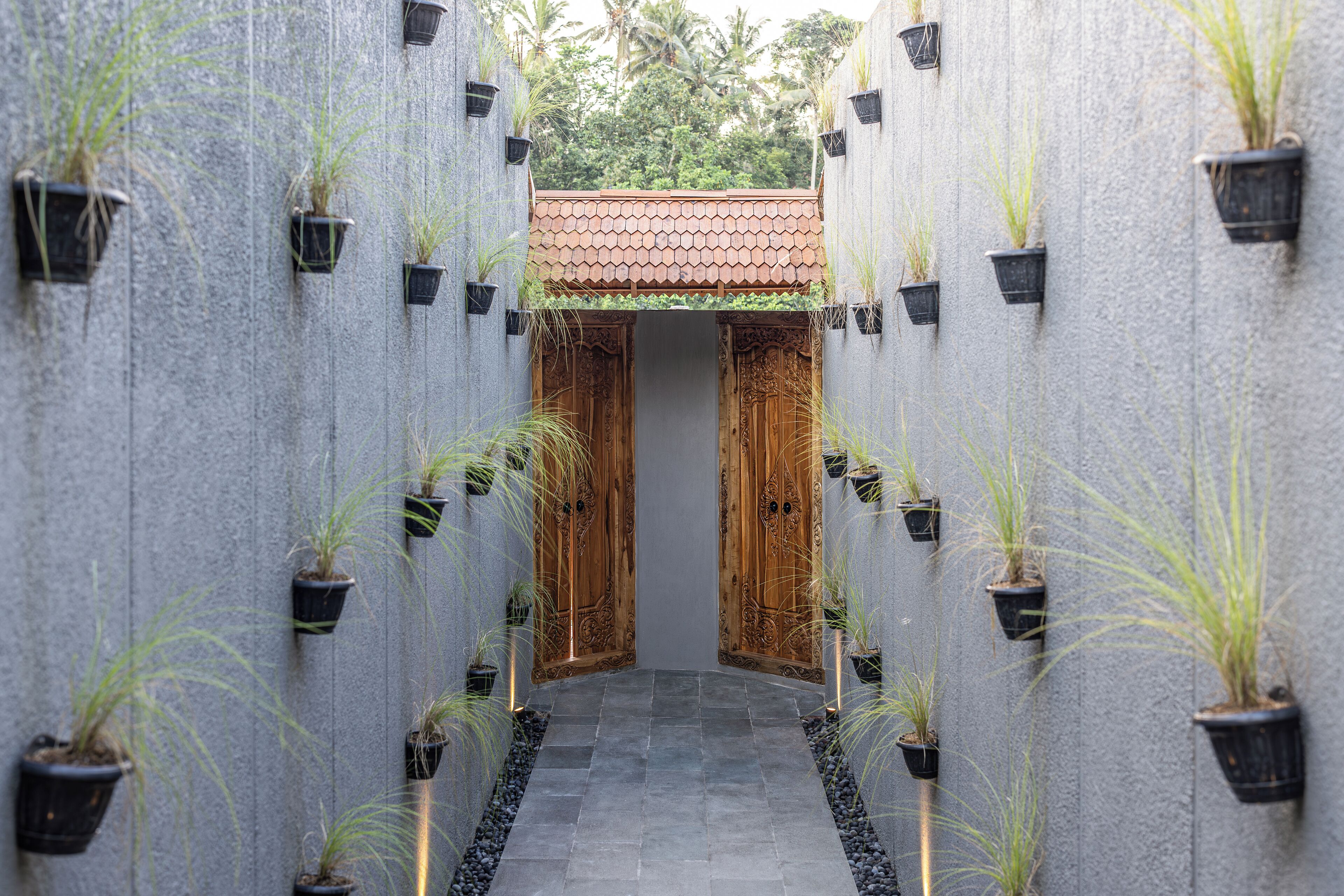 A narrow pathway flanked by vertical walls with potted plants and a tiled roof overhead.