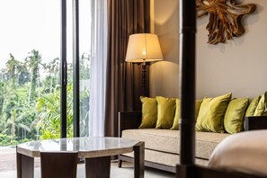 Une chambre d’hôtel avec un canapé, une table et une lampe. La fenêtre donne sur un paysage verdoyant.