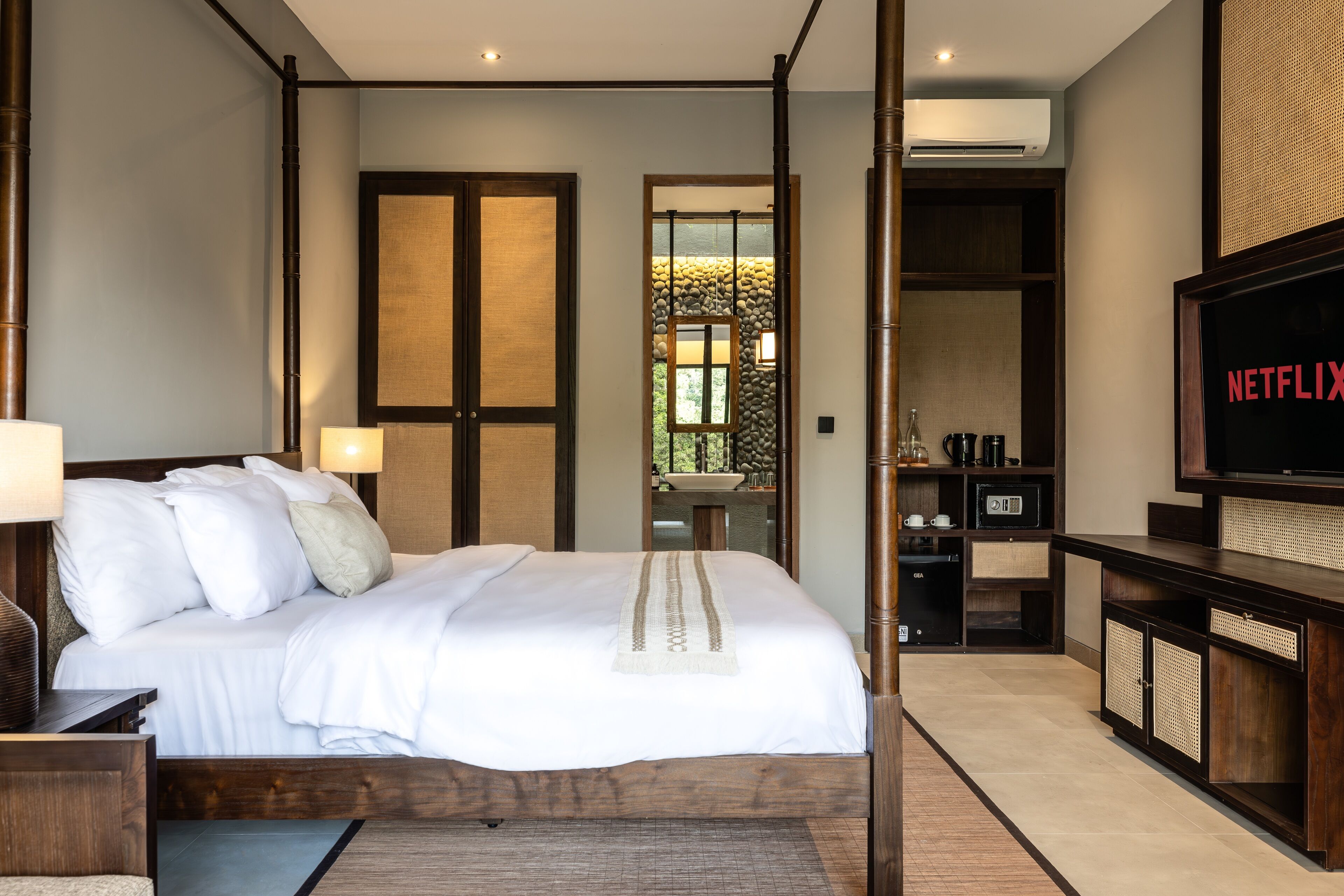 Quarto de hotel moderno com uma cama grande, televisão, minibar e vista para o exterior.