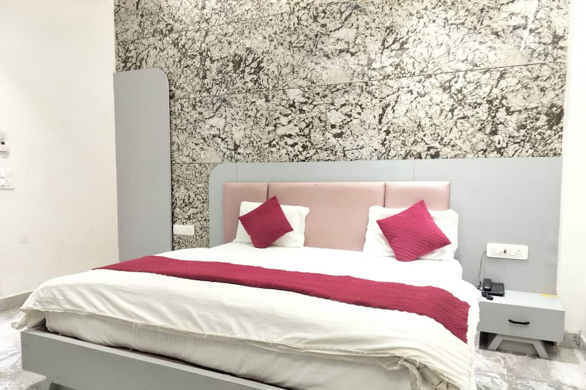 Un dormitorio moderno con cabecera de diseño que imita el mármol, una cama con ropa blanca y una manta roja, y una mesita de noche con un teléfono y cargador.