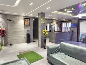 A modern lobby with a reception desk, a sofa, and a vase with sunflowers. - ShrI Balaji Dham (Vrindavan)