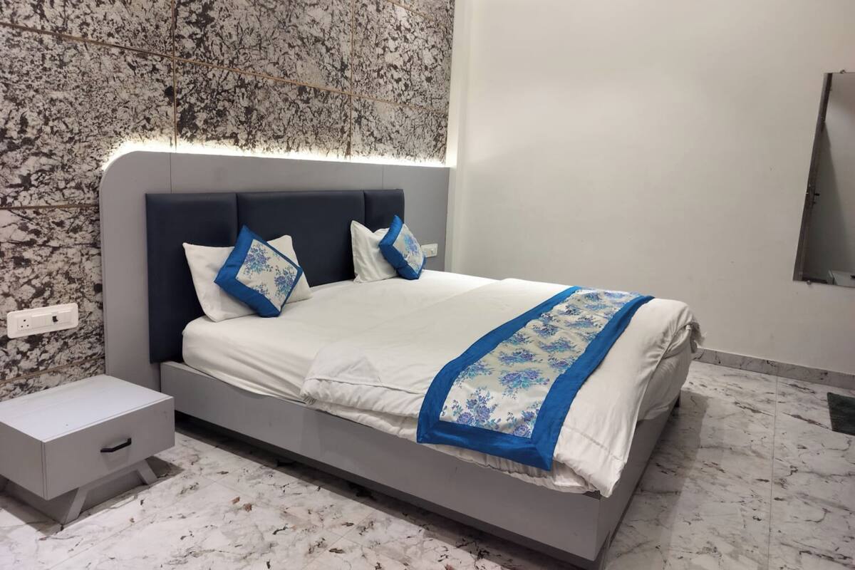 Un dormitorio moderno con piso de mármol, una cama con colcha floral azul y blanca, y una mesita de noche.
