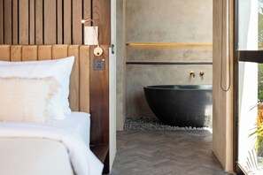 Een moderne slaapkamer met een groot bed, een houten hoofdeinde, een ruime zwarte badkuip en een vloer met een visgraatmotief.