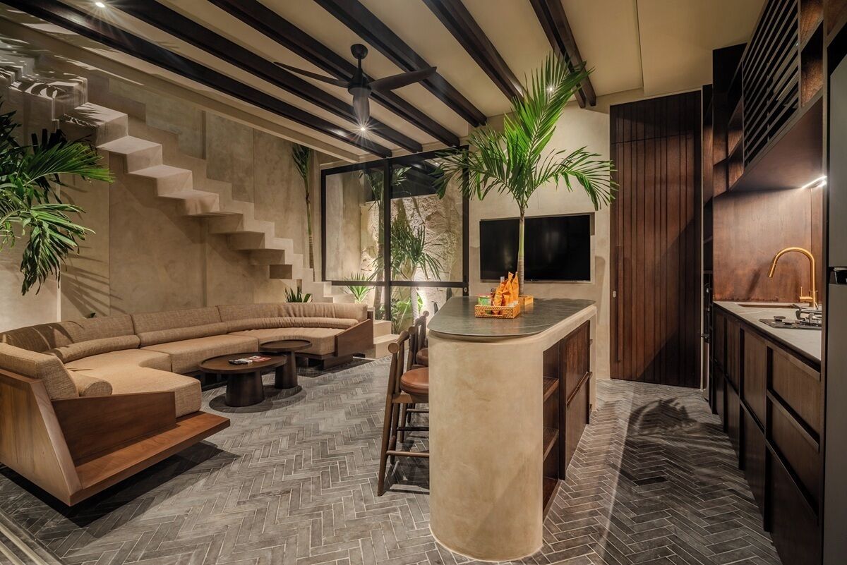 Un intérieur moderne avec un parquet à motifs en chevrons, un canapé incurvé, un îlot central doté d’un évier et un escalier adossé à un mur en pierre.