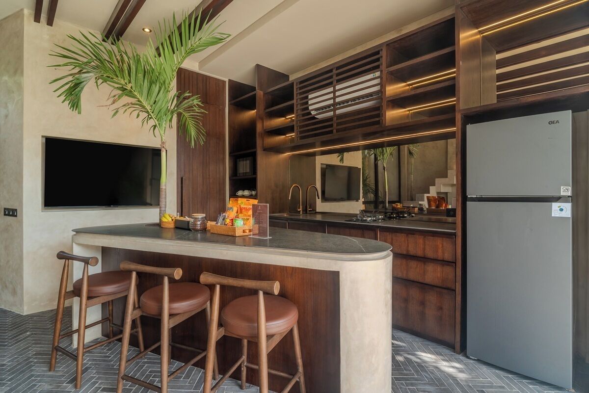 Een moderne keuken met een centraal eiland, barstoelen, een grote flatscreen-tv en een koelkast.