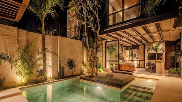 Un espace piscine intérieur moderne, doté d’un salon, de coins détente et de plantes tropicales.