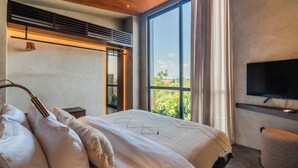 Une chambre d’hôtel moderne dotée d’un grand lit, d’un téléviseur à écran plat et offrant une vue sur la verdure environnante.
