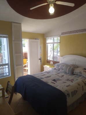 A bedroom with a bed, a ceiling fan, a window, and a door.