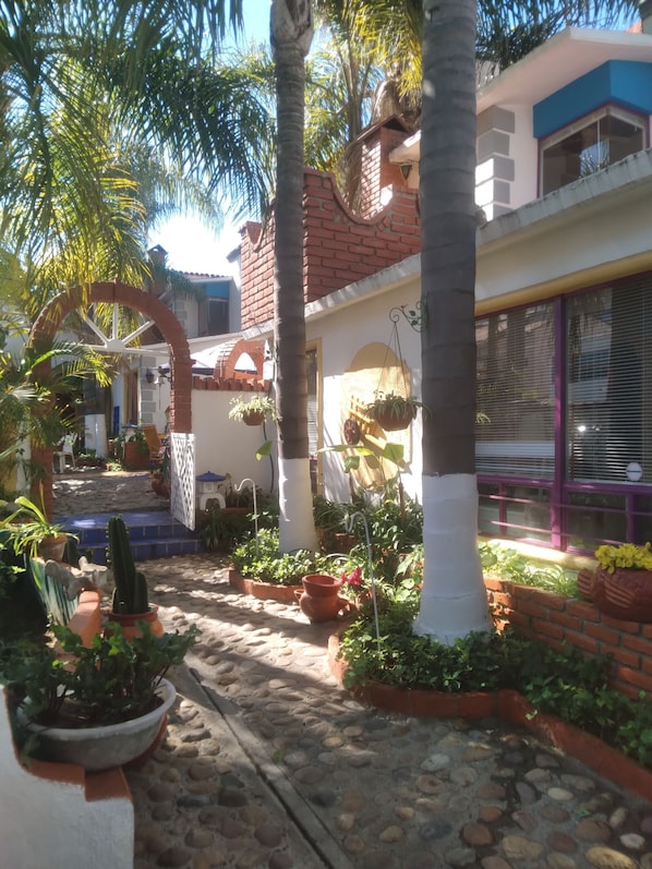 A courtyard with a stone pathway, potted plants, and a brick wall.