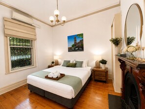A bedroom with a bed, bedside tables, a mirror, a picture on the wall, and a window with a view.