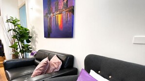 A modern living room with a black leather sofa, a purple pillow, and a cityscape painting on the wall. - Rare 3 Parking! Amazing City Views, CBD at Doorsteps, 3BR2B Beautiful Terrace (West Melbourne)