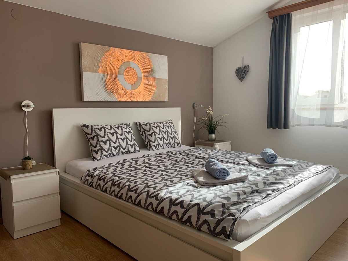 Un dormitorio moderno con cama, mesita de noche, un cuadro en la pared y una ventana con cortinas.