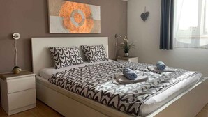 Un dormitorio moderno con cama, mesita de noche, un cuadro en la pared y una ventana con cortinas.