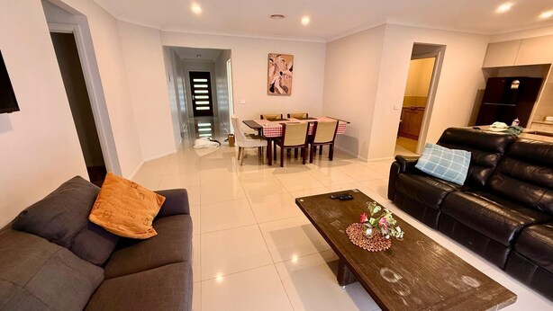 Un salon moderne avec un canapé, une table basse agrémentée de fleurs, un coin repas avec une table et des chaises, et un divan en cuir noir.