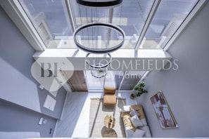 A modern, well-lit room with a skylight, a round table, a sofa, and a framed picture on the wall. - Bloomfields 1BR in Rukan Lofts-Wadi Al Safa 7 (Dubai)