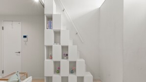 A modern staircase with white steps and a handrail, leading to a landing with a white door and a small control panel. - ANON Shibuya A103 (Tokyo)