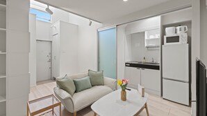 A modern, open-plan living space with a sofa, coffee table, and kitchen area including a microwave and refrigerator. - ANON Shibuya A103 (Tokyo)