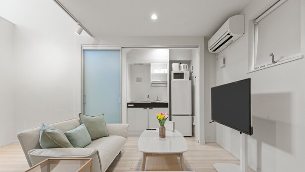 A modern living room with a sofa, coffee table, and TV. There is a kitchen area with a fridge and microwave. - ANON Shibuya A103 (Tokyo)