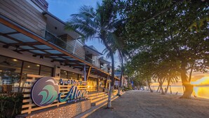 Un hôtel situé en bord de mer, avec une enseigne indiquant « Jparis Island Resort » et « Alona », et présentant un design moderne avec un balcon donnant sur la plage.