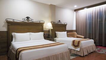 A hotel room with two beds, a chair, a lamp, and a window with curtains.